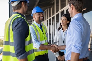 African American man in a hard hat shaking hands with a man and a woman gathered around a construction site